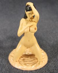 Erotic figurine of a nude female, kneeling on the red silk sheet.